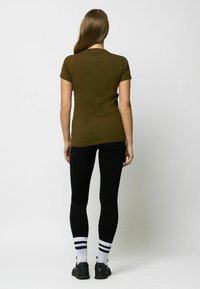 Olijfgroen fitted t-shirt met korte mouwen, gecombineerd met zwarte leggings en zwarte sportschoenen. Witte sokken met zwarte strepen.