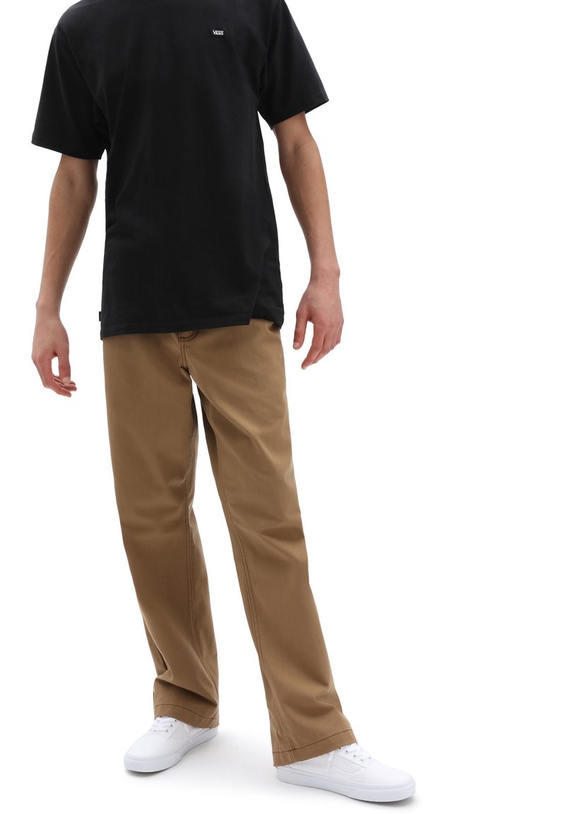 Svart kortärmad t-shirt med logotyp, kombinerad med beige raka byxor och vita sneakers, vilket framhäver den avslappnade designen och tygtexturen.