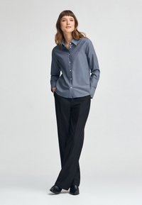 Camicia azzurra chiaro con colletto a punte e maniche lunghe, abbinata a pantaloni neri a gamba dritta e scarpe nere.