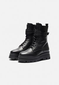 Bottes de combat en cuir noir avec design à lacets, hauteur au niveau de la cheville, sangle ajustable, semelle en caoutchouc épaisse et surface texturée.