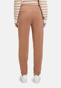 Lichtbruine corduroy broek met een relaxte pasvorm, voorzien van achterzakken en opgerolde manchetten, gecombineerd met witte sneakers. Gestreept sweater zichtbaar erboven.