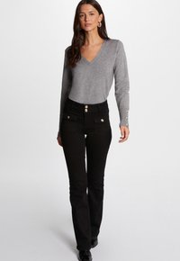 Pull gris à col en V associé à un jean noir taille haute avec trois accents de boutons dorés et deux poches avant. Texture de tissu lisse.