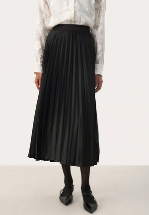 Black pleated skirt with a high waistband, made of a smooth fabric. Ankle-length with a flowing design. Worn with a sheer, textured white blouse.