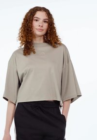 Top corto de manga corta en tejido beige claro con un cuello alto. Presenta un logotipo sutil en el pecho y un corte suelto y relajado.