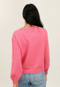 Pull en tricot rose avec de longues manches ballon et un ourlet côtelé. Texture lisse, design col rond, associé à un jean délavé.