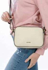 Borsa a tracolla in pelle color crema con forma rettangolare, rifiniture marroni, dettagli in oro e tracolla rimovibile, esposta su uno sfondo chiaro.