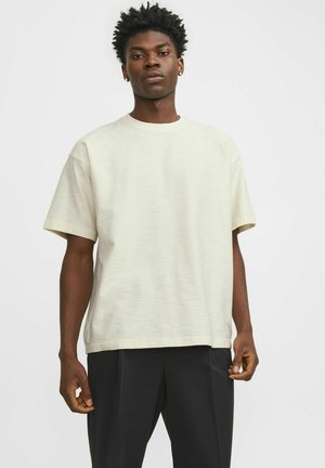 Camiseta de manga corta en color crema con un corte relajado y una superficie texturizada sutil, combinada con pantalones negros holgados.
