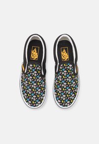 Des chaussures Vans noires à enfiler avec un motif floral coloré et petit, des semelles intermédiaires blanches, et des étiquettes de logo Vans orange sur les côtés et les semelles intérieures.
