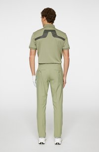 Ljusgrön polo med svart mönsterdetalj på ryggen, i kombination med matchande ljusgröna byxor och vita golfsko.