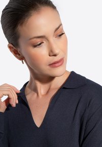 Granatowy sweter z dekoltem w serek i kołnierzykiem. Materiał jest gładki, z luźnymi rękawami i subtelną teksturą. Widoczne złote kolczyki w kształcie kół.