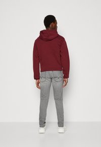 Sudadera color marrón con una gran capucha, que presenta una textura suave. Combinada con jeans gris claro, que muestran un ajuste ceñido y sutilezas en la costura.