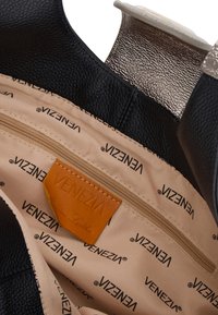 Wnętrze czarnej skórzanej torebki z kieszonką na zamek, w beżowym wykończeniu z powtarzającym się logo "Venezia" oraz beżową skórzaną metką. Srebrne detale.
