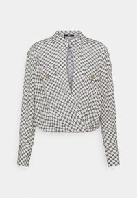 Hvid langærmet bluse med sort sammenflettet kædemønster, to brystlommer med knap og plisseret detalje ved kraven og kanten.