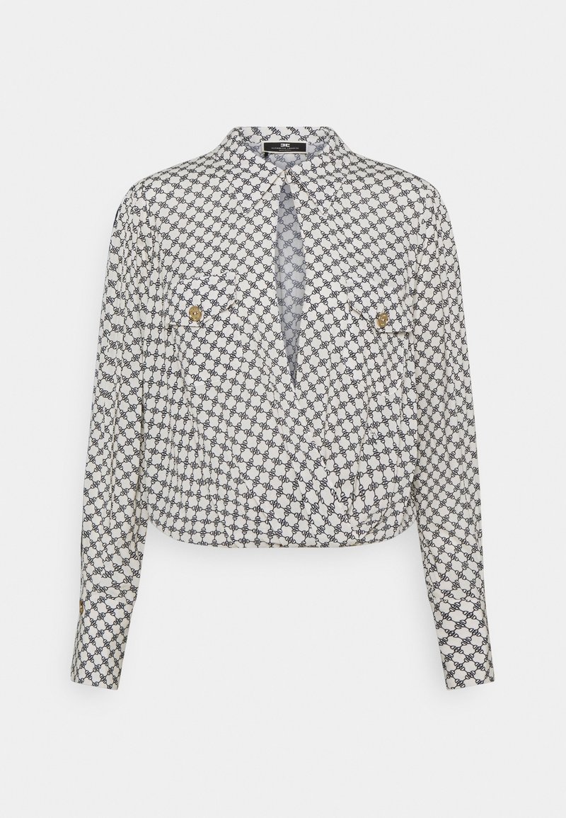 Hvid langærmet bluse med sort sammenflettet kædemønster, to brystlommer med knap og plisseret detalje ved kraven og kanten.