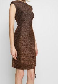 Brun, glittrig klänning med en figurnära design, korta ärmar och sidofästa detaljer. Den släta texturen förbättrar reflekterande egenskaper.