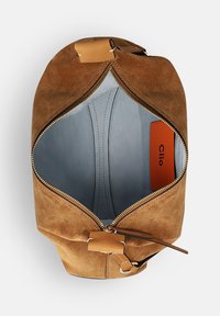 Braune Wildledertasche mit einem Reißverschluss, ausgestattet mit einem hellblauen Innenfutter und einem orangefarbenen Logoschild. Akzente bilden braune Lederbeschläge.