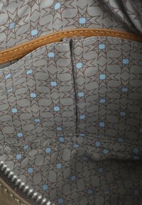 Interno di una borsa in tessuto marrone, caratterizzato da un rivestimento grigio chiaro con un motivo di stelle marroni e blu, e un accentuazione in pelle beige lungo il bordo superiore.