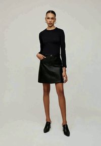 Μαύρη μπλούζα με μακριά μανίκια και μαύρη μίνι φούστα από δερμάτινο υλικό ψηλόμεση. Η φούστα έχει υφή με διακριτό σχέδιο. Μαύρες ψηλοτάκουνες μούλες.