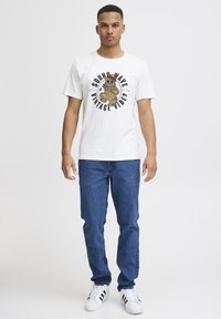Hvit bomulls T-skjorte med grafisk trykk av en bjørn og teksten "SOUND WAVE VINTAGE VIBES". Kombinert med blå denimjeans og hvite sneakers.