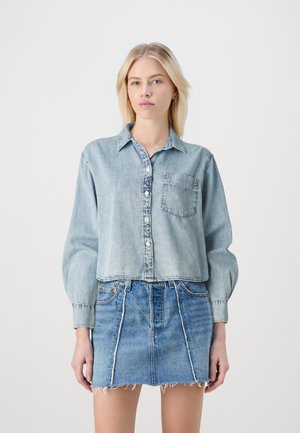 Lichtblauwe denim cropped shirt met knoopsluiting, lange mouwen en een enkele borstzak. Gepaard met een vervaagde denim mini-jurk met een rafelige zoom.