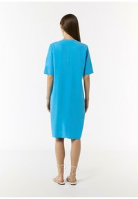 Blaues kurzärmliges Kleid mit lockerer Passform, knielangem Design und geradem Rückennaht; getragen mit beigen Schnürsandalen.