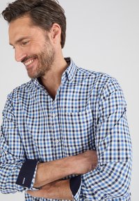Camicia a maniche lunghe a quadri con quadrati blu e bianchi, con polsini blu scuro e una tasca sul petto. Tessuto di cotone liscio.