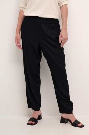 Pantalons noirs à coupe décontractée en tissu lisse, avec une taille élastique. Associés à des sandales noires à enfiler et un haut crème texturé.