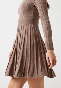Abito in maglia di un marrone tenue, caratterizzato da una texture a costine, maniche lunghe, un corpetto aderente e una gonna a pieghe svasata.