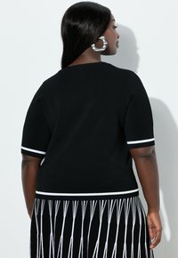 Zwarte gebreide top met korte mouwen, met witte streepaccenten aan de mouwen en zoom, gecombineerd met een zwarte rok met witte franjes.