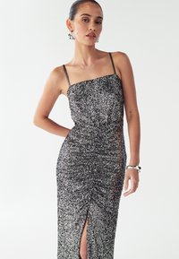 Zwart-zilveren jurk met pailletten, rechte halslijn, dunne bandjes, zijsplit en geplooide textuur op het lijfje en de rok.