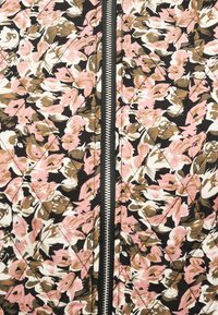 Gros plan sur un tissu à motif floral avec des feuilles roses, marron et blanches, présentant une fermeture éclair centrale argentée sur une bordure noire.