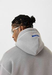 Grijze hoodie met een textuurfinish, met een blauw label op het achterste nekgebied. Het ontwerp omvat een grote, oversized pasvorm.
