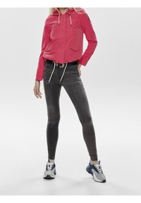 Rosa Kapuzenjacke mit Fronttaschen, kombiniert mit schwarzen Skinny Jeans und blau-grauen Sneakers. Fokus auf einem lässigen, sportlichen Look.