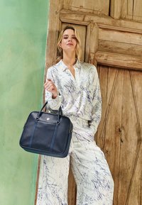 Navy leather tote bag with dual top handles, featuring contrast stitching and a gold logo, placed against a textured wooden background.