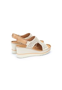Sandali wedge leggeri con tomaia perforata color crema, dettagli in marrone e soletta imbottita. Presentano una cintura posteriore regolabile per una vestibilità sicura.