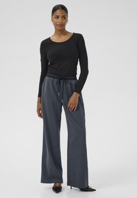 Zwarte langemouwen top, gecombineerd met losse, donkerblauwe denim broeken met een elastische tailleband en strikdetail.