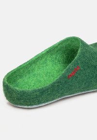 Pantofole verdi in feltro dalla forma arrotondata, con superficie testurizzata e un logo rosso. La fodera interna si abbina al colore esterno, offrendo un aspetto uniforme.