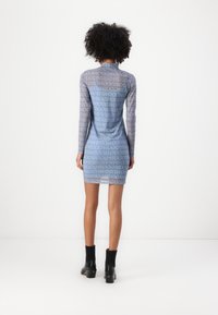 Langdurige, aansluitende jurk van doorschijnende blauwe stof met herhaald logo-patroon. Gestyled met zwarte blokhakken enkellaarsjes.