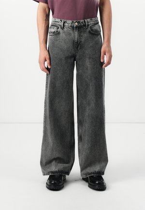 Wide-leg jeans in faded black denim. Features a zip fly, five pockets, and contrast stitching. Paired with black chunky shoes.