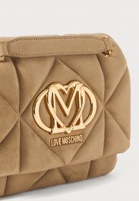Borsa a tracolla beige trapuntata in morbido suede con logo in metallo color oro che presenta lettere intrecciate. Chiusura semplice con patta e tracolla.