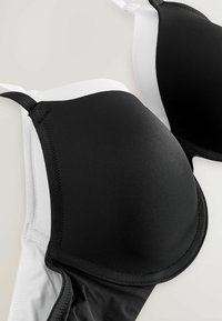 Zwart-witte molded cup beha's hebben een gladde stof, verstelbare bandjes en contrasterende kleuren, met stiksels die de cups omlijsten.