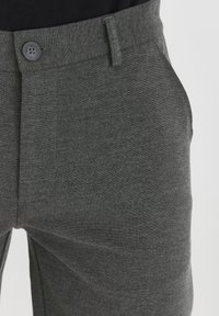 Close-up of gray pants with a button and belt loop, worn over a black top, highlighting the fabric texture and fit.