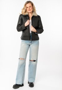 Zwarte leren jas met een nepbont kraag, ritsluiting en zijzakken, gecombineerd met lichtblauwe gescheurde jeans en zwarte chunky laarzen.