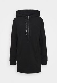 Sudadera negra con capucha, hecha de una tela suave, que cuenta con cierre de cremallera, cordones y un corte relajado con mangas largas. Costuras planas visibles.