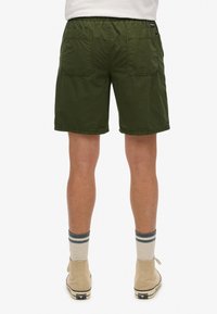 Pantalones cortos verdes con cintura elástica, dos bolsillos traseros y un diseño recto. Combinados con zapatos de caña alta beige y calcetines a rayas.