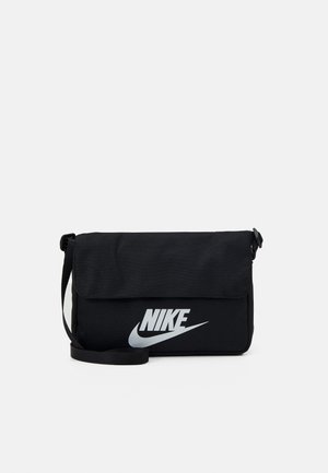 Črna tkaninska torba preko rame z zapiranjem na pokrov, ki ima na sprednji strani izstopajoč srebrni Nike logotip in nastavljiv trak.