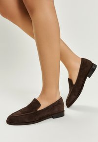 Loaferi din suede maro, cu un toc mic tip bloc, având un vârf rotund și un design decupat pe partea superioară. Textură moale și finisaj neted.