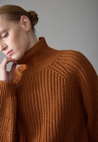 Knitted turtleneck sweater in rich orange, featuring textured stitch patterns, wide sleeves, and a high collar for warmth.