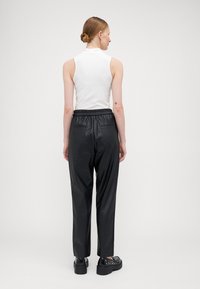 Haut sans manches blanc et pantalon en simili cuir noir avec ceinture élastique et poches arrière, associés à des chaussures noires à semelles épaisses avec clous.
