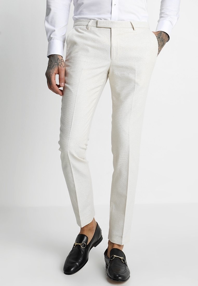 Vaaleanbeige slim-fit-housut, joissa on teksturoitu kuvio, litteä etuosa, sivutaskut ja vyölenkit, yhdistettynä mustiin loafereihin.